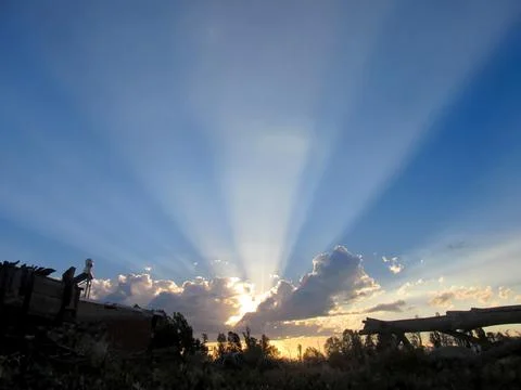 Sun rays piercing through dramatic clouds during a stunning countryside sunse Stock Photos
