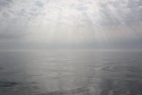 Sun rays shine onto calm and misty sea Stock Photos