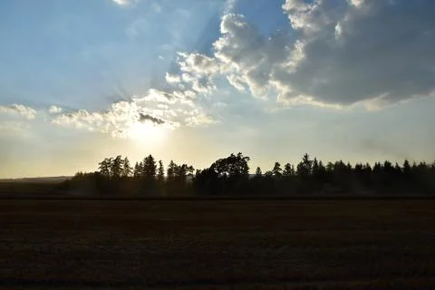 The sun rays shine from the clouds over the field where the harvester cuts. T Stock Photos