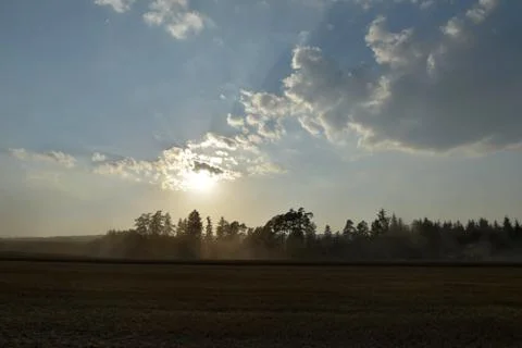 The sun rays shine from the clouds over the field where the harvester cuts. T Stock Photos