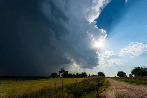 Sun rays shine through storm clouds over a quiet country road, creating a dra Stock Photos