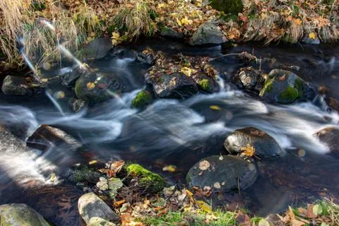Sun rays shine on a water cascade in the brook. Stock Photos