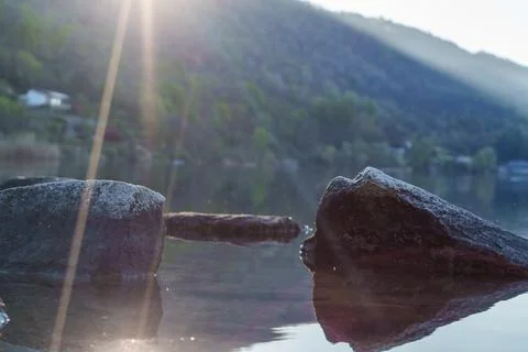 Sun rays shining on rocks by calm lake Stock Photos
