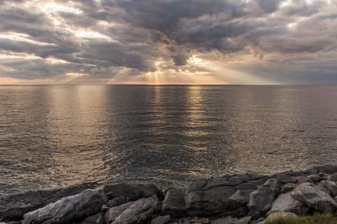 Sun rays shining through clouds over the ocean Stock Photos