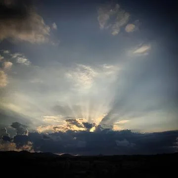 Sun rays shining through clouds in a bright sky Stock Photos
