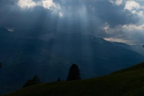 Sun rays shining trough the clouds in the mountains, a hill and trees in fron Stock Photos