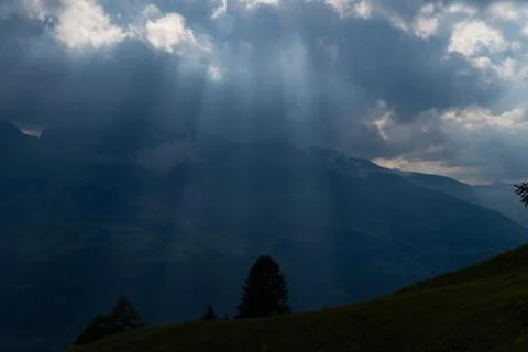 Sun rays shining trough the clouds in the mountains, a hill and trees in fron Stock Photos