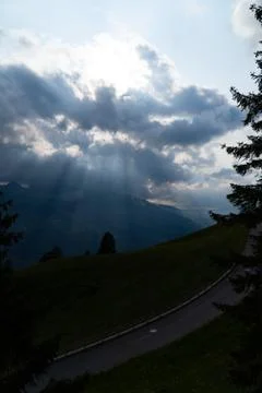 Sun rays shining trough the clouds in the mountains, a hill, a street and tre Stock Photos