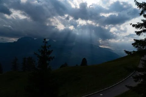 Sun rays shining trough the clouds in the mountains, a hill, a street and tre Stock Photos