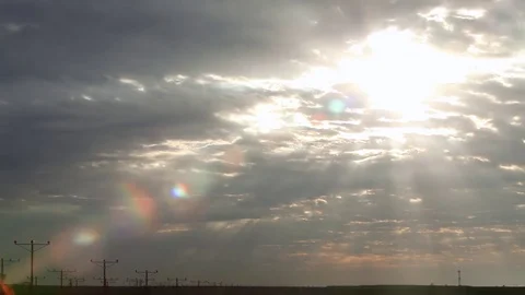 Sun rays shinning through dramatic clouds behind a line of electrical posts Stock Footage 80440058