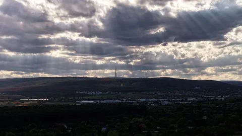 Sun rays stream through layered dramatic clouds above rolling wooded hills and Stock Footage 345336354