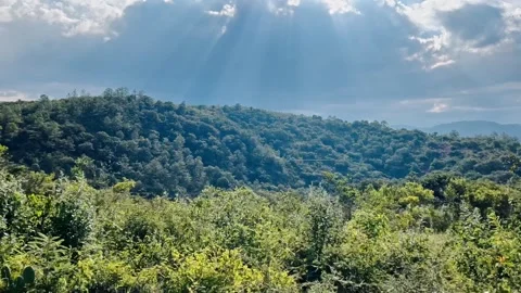 Sun Rays Streaming Through Clouds Over Forested Hills and Green Countryside Vidéo 348985046