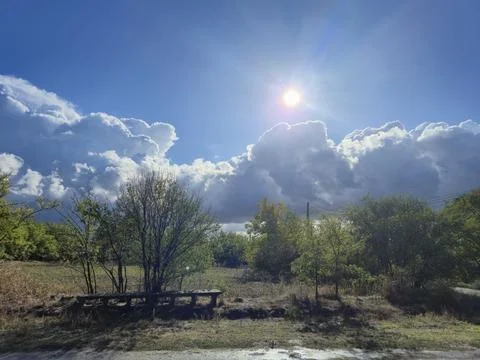 Sun Rays Through Partly Cloudy Sky Over Green Trees in Countryside Stock Photos
