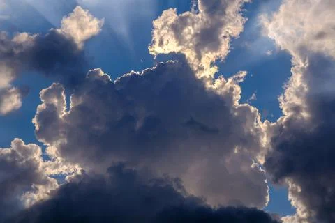 Sun rays in the white high cumulus clouds in the clear blue sky Stock Photos