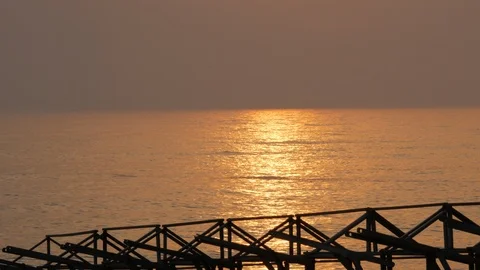 Sun reflected on ocean surface at sunset with beach hut frames in silhouette Stock Footage 111880428