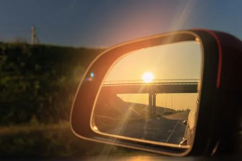 The sun is reflected in the side rear view mirror, evening road. Stock Photos