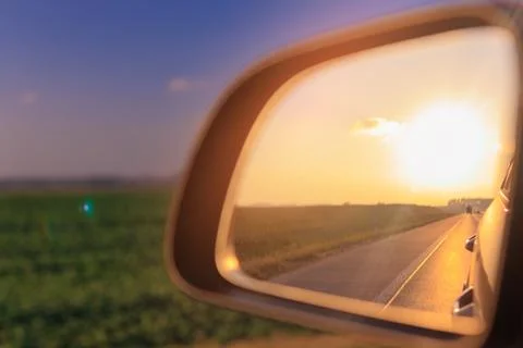 The sun is reflected in the side rear view mirror, evening road. Stock Photos
