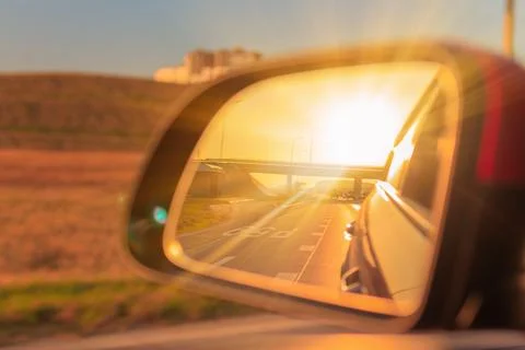 The sun is reflected in the side rear view mirror, evening road. Stock Photos
