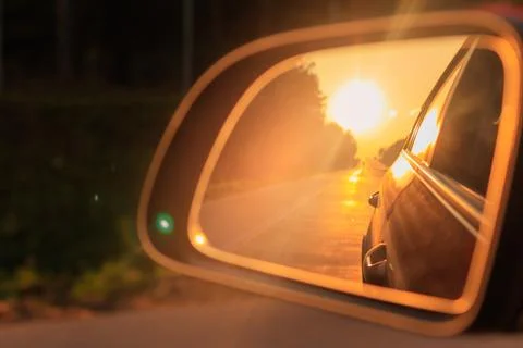 The sun is reflected in the side rear view mirror, evening road. Stock Photos