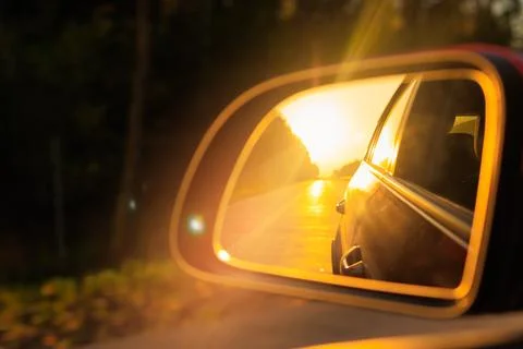 The sun is reflected in the side rear view mirror, evening road. Stock Photos