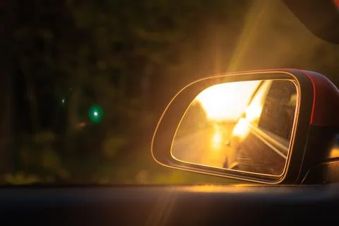 The sun is reflected in the side rear view mirror, evening road. Stock Photos
