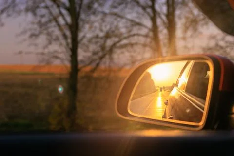 The sun is reflected in the side rear view mirror, evening road. Stock Photos