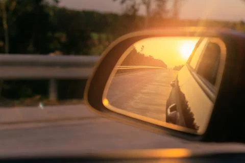 The sun is reflected in the side rear view mirror, evening road. Stock Photos