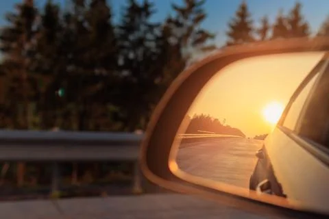 The sun is reflected in the side rear view mirror, evening road. 库存照片