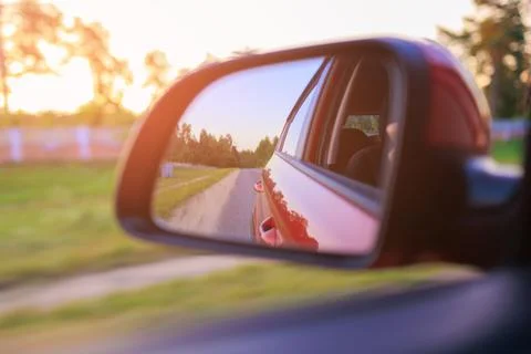 The sun is reflected in the side rear view mirror, evening road. Stock Photos