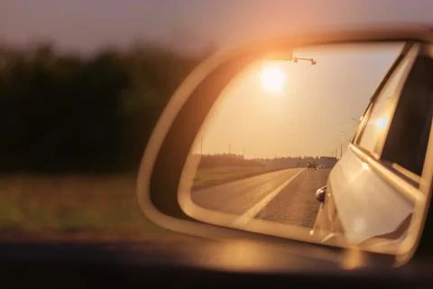 The sun is reflected in the side rear view mirror, evening road. Stock Photos