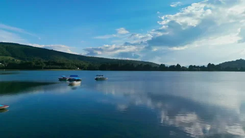 Sun reflecting on a calm reservoir surrounded by forested hills at golden hour Stock Footage 346014707