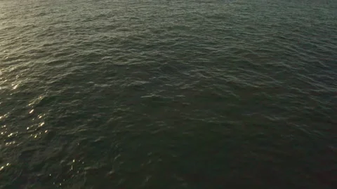 Sun reflecting off ocean drone pull back and tilt up to reveal sea Stock Footage 167475171