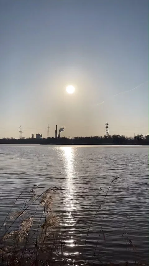 Sun Reflecting on River with Industrial Skyline and Smoking Chimneys at Sunset Видео 336765631
