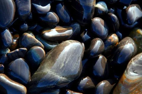 Sun reflections on round and oval shaped black and brown stones on the beach Stock Photos
