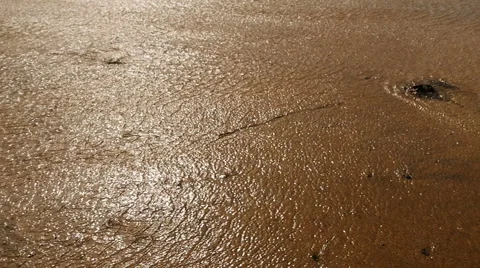 Sun reflects off patterns in shallow waves on beach Stock Footage 56081116