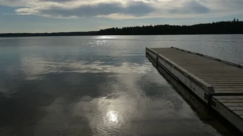 The sun reflects on the water of a large calm lake with a long wooden pier.   Stock Footage 156516427