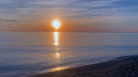 Sun rises above calm sea, casting golden reflection across gentle waves and Stock Footage 337777126