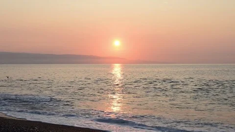 The sun rises on the beach of Taormina while the waves break on the shoreline Stock Footage 83914375