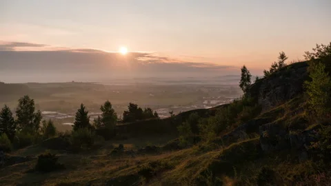Sun rises behind clouds and illuminates urban area with green foreground Stock Footage 221583417