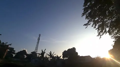 The sun rises behind a quiet suburban scene with a telecom tower Video stock 311365216