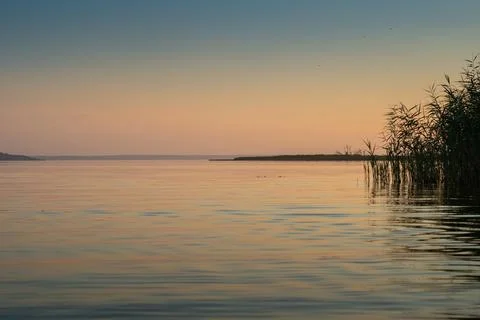 The sun rises or sets over a river with thickets of reeds. Foto stock