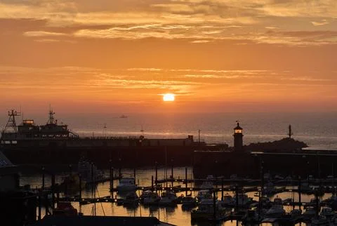 The sun rises in an orange sky over the silhouette Ramsgate harbour Stock Photos