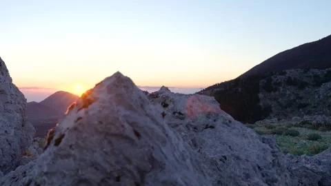 The sun rises over a mountain behind some rocks Stock Footage 289139535