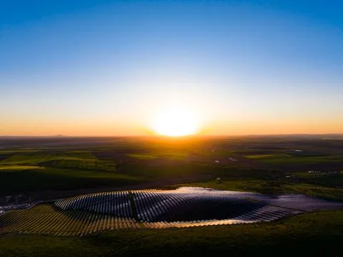 The sun rises over solar panels situated in a rural area. The landscape inclu Stock Photos