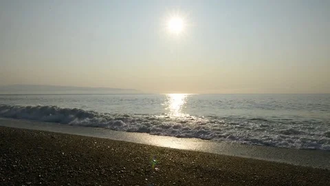 The sun rises from the sea on a hot summer day with the waves on the beach Video stock 84007386