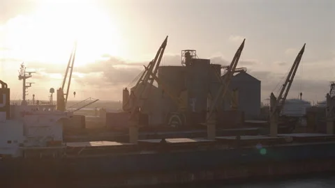 Sun rising over a bulk carrier vessel with cranes loading grain from silos in a Stock Footage 345524974