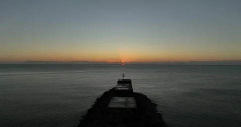 Sun rising over an empty sea with a harbour arm in the foreground Stock Footage 345584742