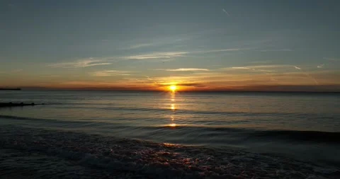 Sun rising over gentle waves lapping at the shore Stock Footage 345584748