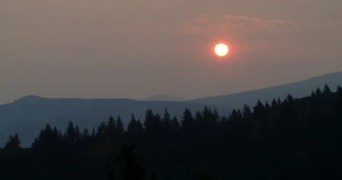 Sun rising through clouds in a smoky sky with forest and mountains Stock Footage 104455029