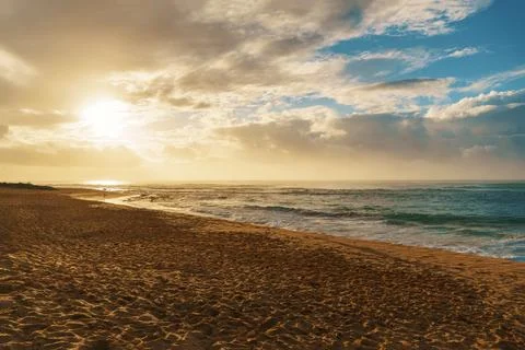 The sun sets above the ocean on a cloudy day at the beach Stock Photos